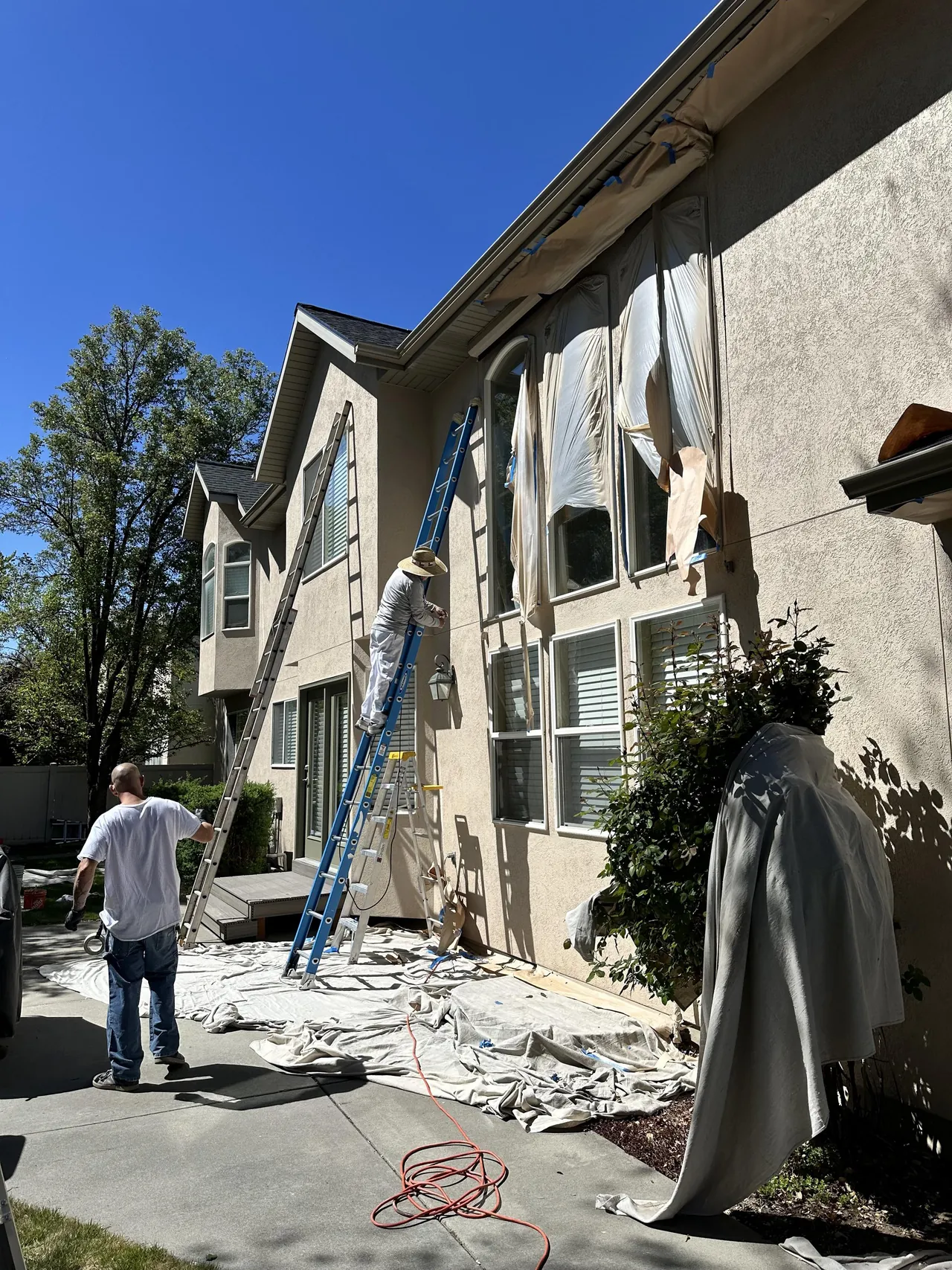 Painting crew on ladders repainting a two-story stucco home