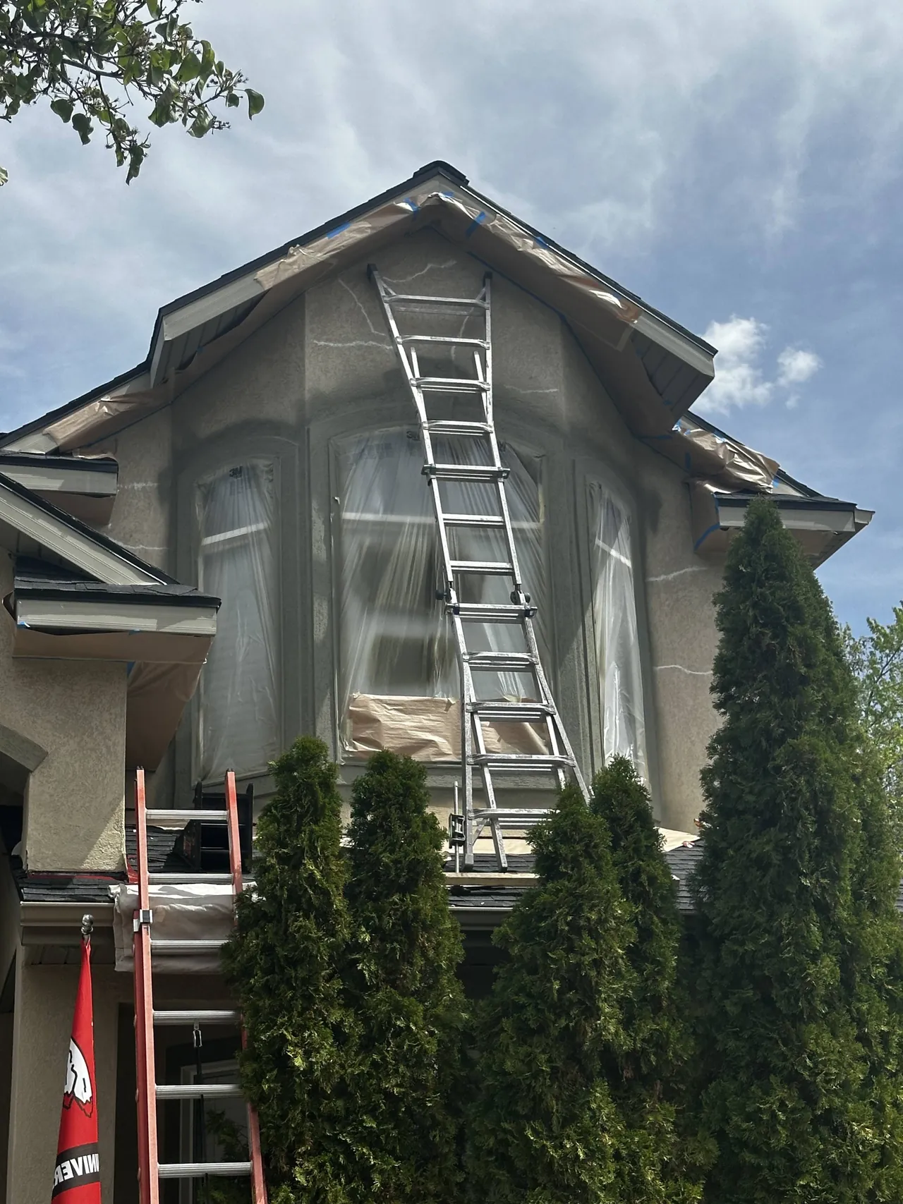 Ladder set against a bay window masked with plastic during exterior painting prep