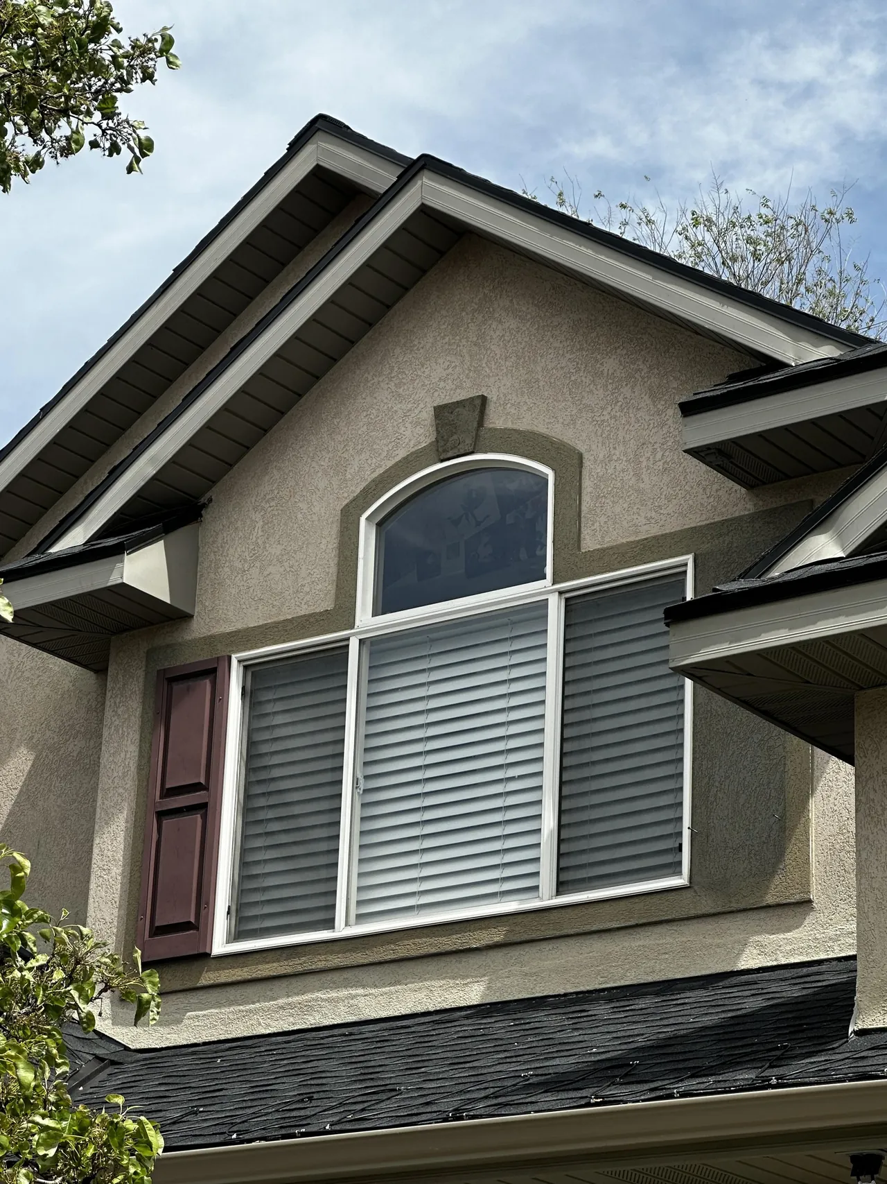 Repainted stucco gable with arched window and maroon shutters